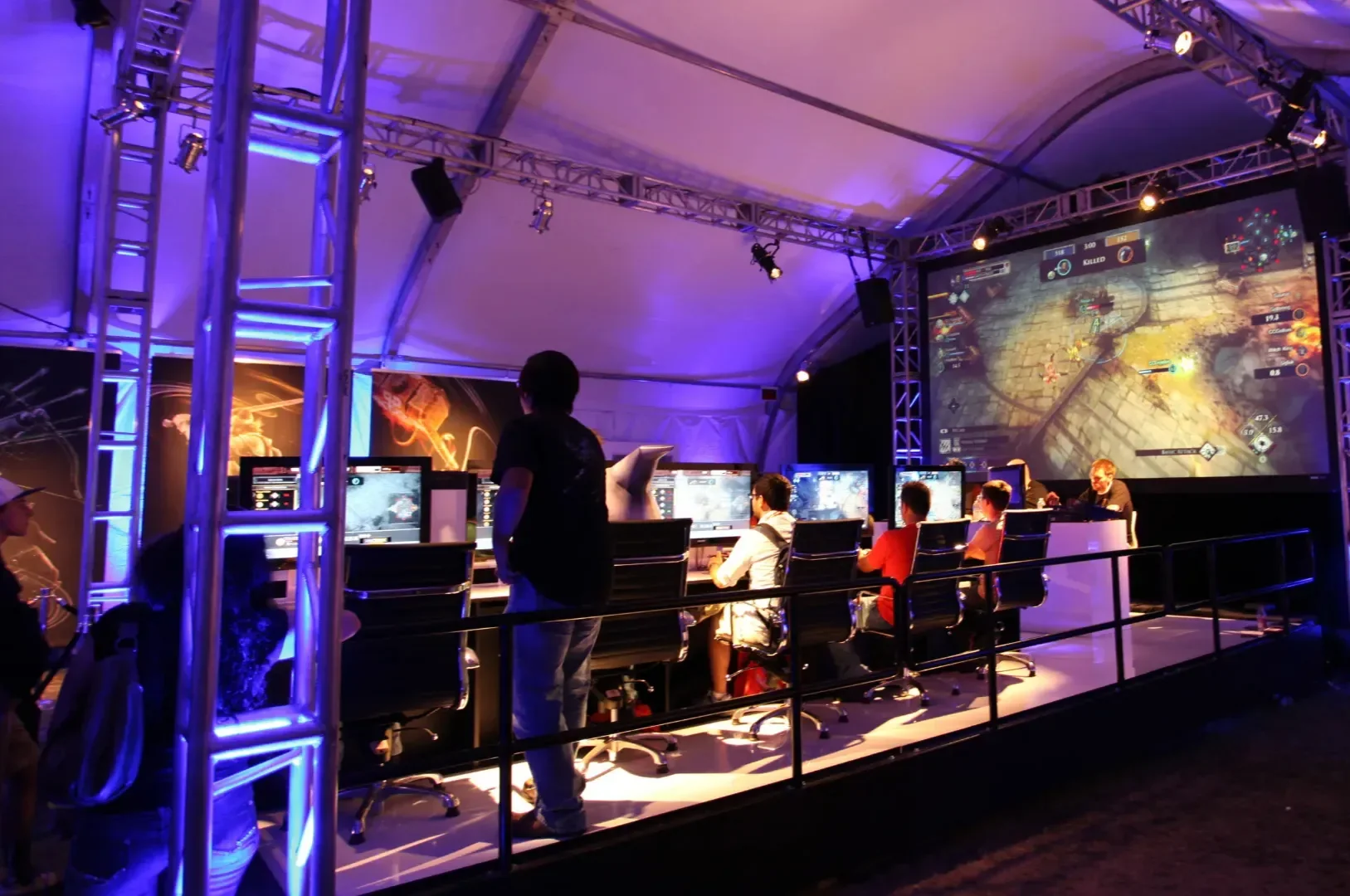 Gaming tournament stage: rows of players under truss lights and a giant screen